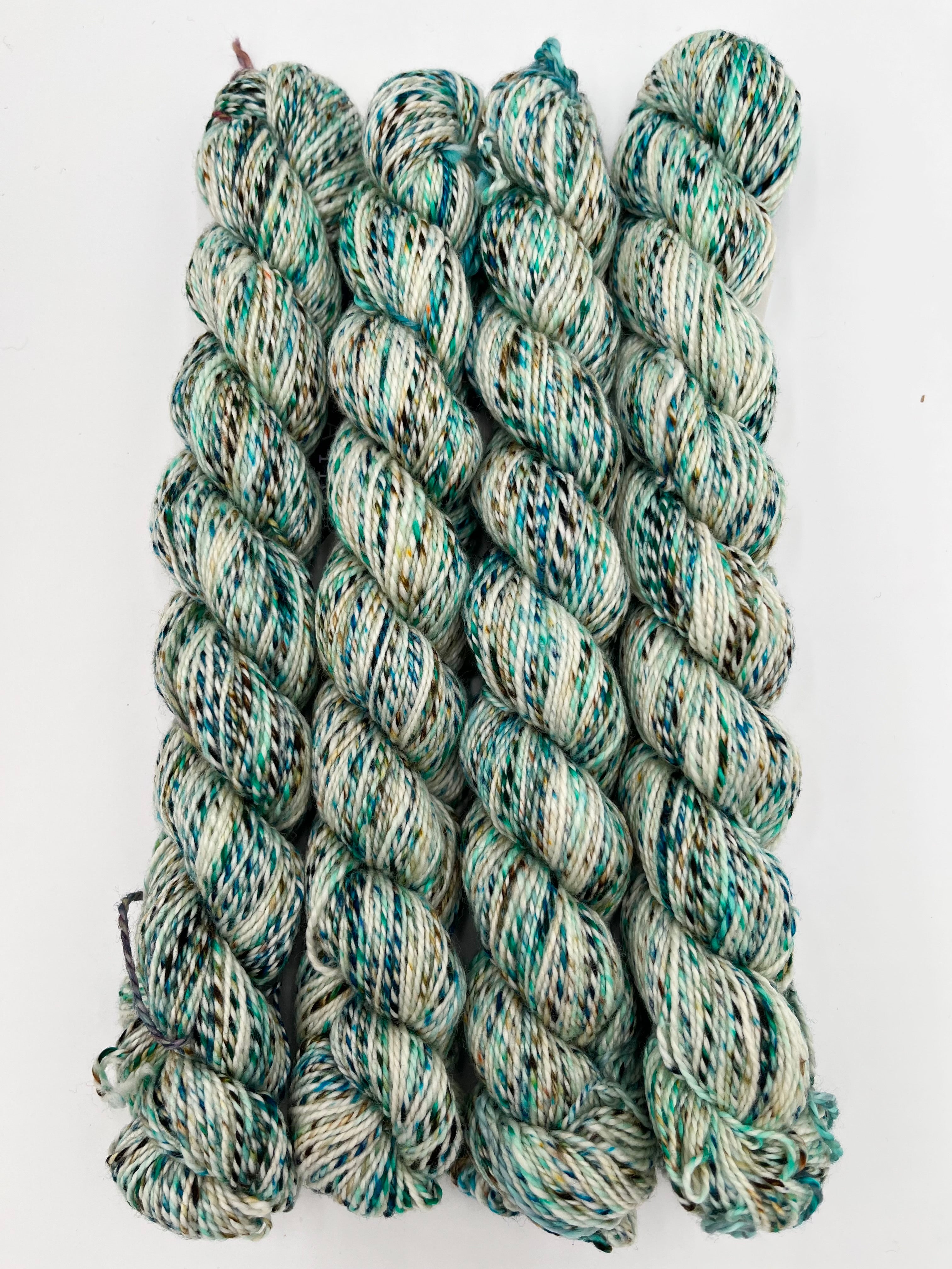 Four twisted skeins of variegated yarn with a marled pattern of teal, green, cream, and off-white, arranged vertically on a plain white background.