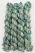 Four twisted skeins of variegated yarn with a marled pattern of teal, green, cream, and off-white, arranged vertically on a plain white background.