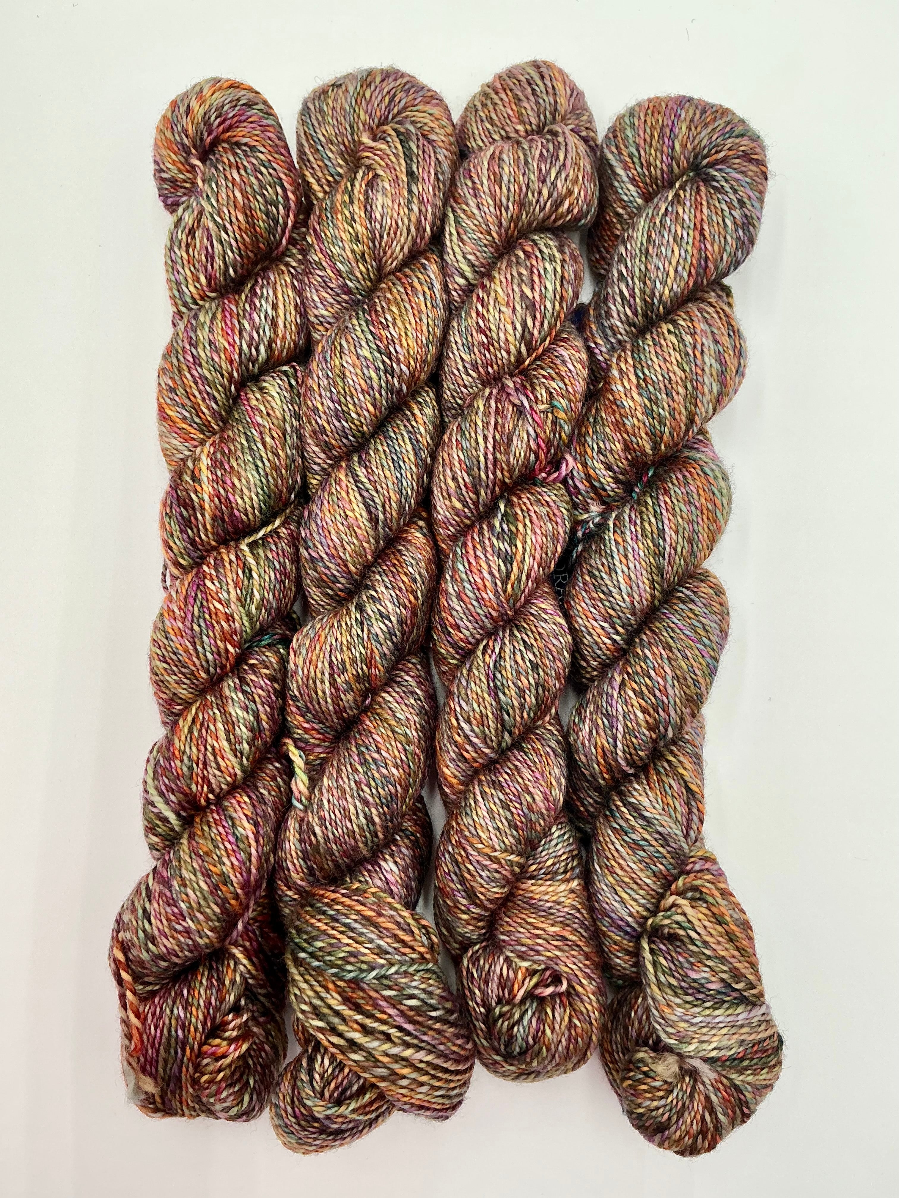 Four skeins of variegated yarn with a heathered, twisted texture in earthy brown, beige, and muted red tones, arranged vertically on a plain white background.