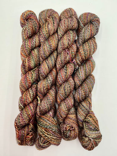 Four skeins of variegated yarn with a heathered, twisted texture in earthy brown, beige, and muted red tones, arranged vertically on a plain white background.
