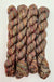 Four skeins of variegated yarn with a heathered, twisted texture in earthy brown, beige, and muted red tones, arranged vertically on a plain white background.