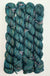 Four skeins of variegated yarn in a heathered teal, green, and blue colorway, arranged vertically on a plain white background.