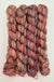 Four twisted skeins of variegated yarn, with a multicolor blend of red, orange, pink, green, and cream tones, arranged on a white background.