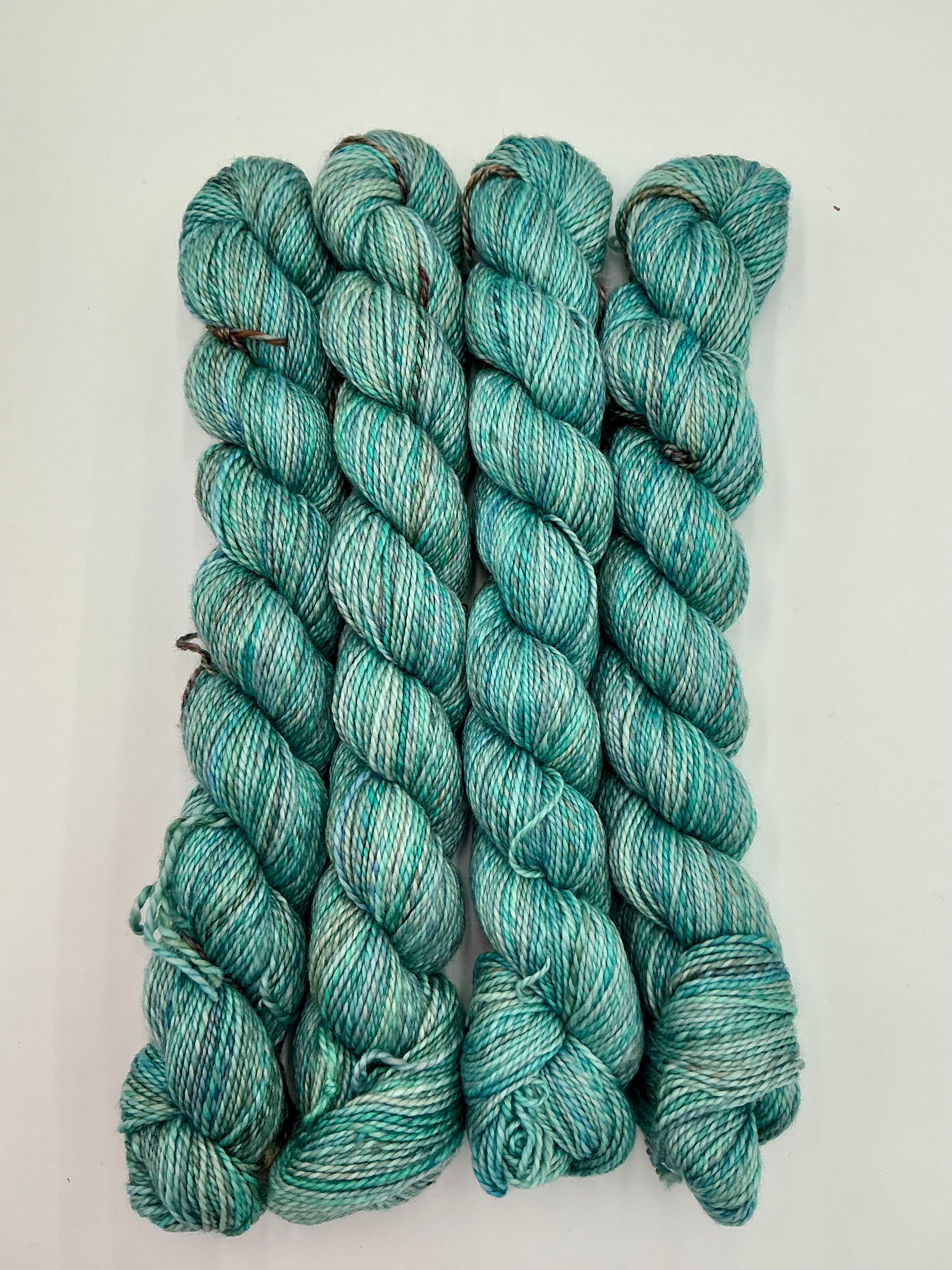 Four skeins of variegated teal, blue, and  mint green yarn, arranged vertically on a plain white background.