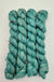 Four skeins of variegated teal, blue, and  mint green yarn, arranged vertically on a plain white background.