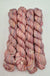 Four skeins of variegated yarn in dusty pink, mauve, and cream tones, arranged vertically on a white background.