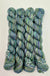 Four skeins of variegated yarn with a blend of blue, green, and purple tones, arranged vertically on a white background.