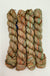 Four skeins of variegated yarn in earthy shades of beige, brown, muted green, and orange, arranged vertically on a plain white background.