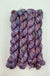 Four skeins of variegated yarn in shades of purple, pink, red, and black, arranged vertically on a plain white background.