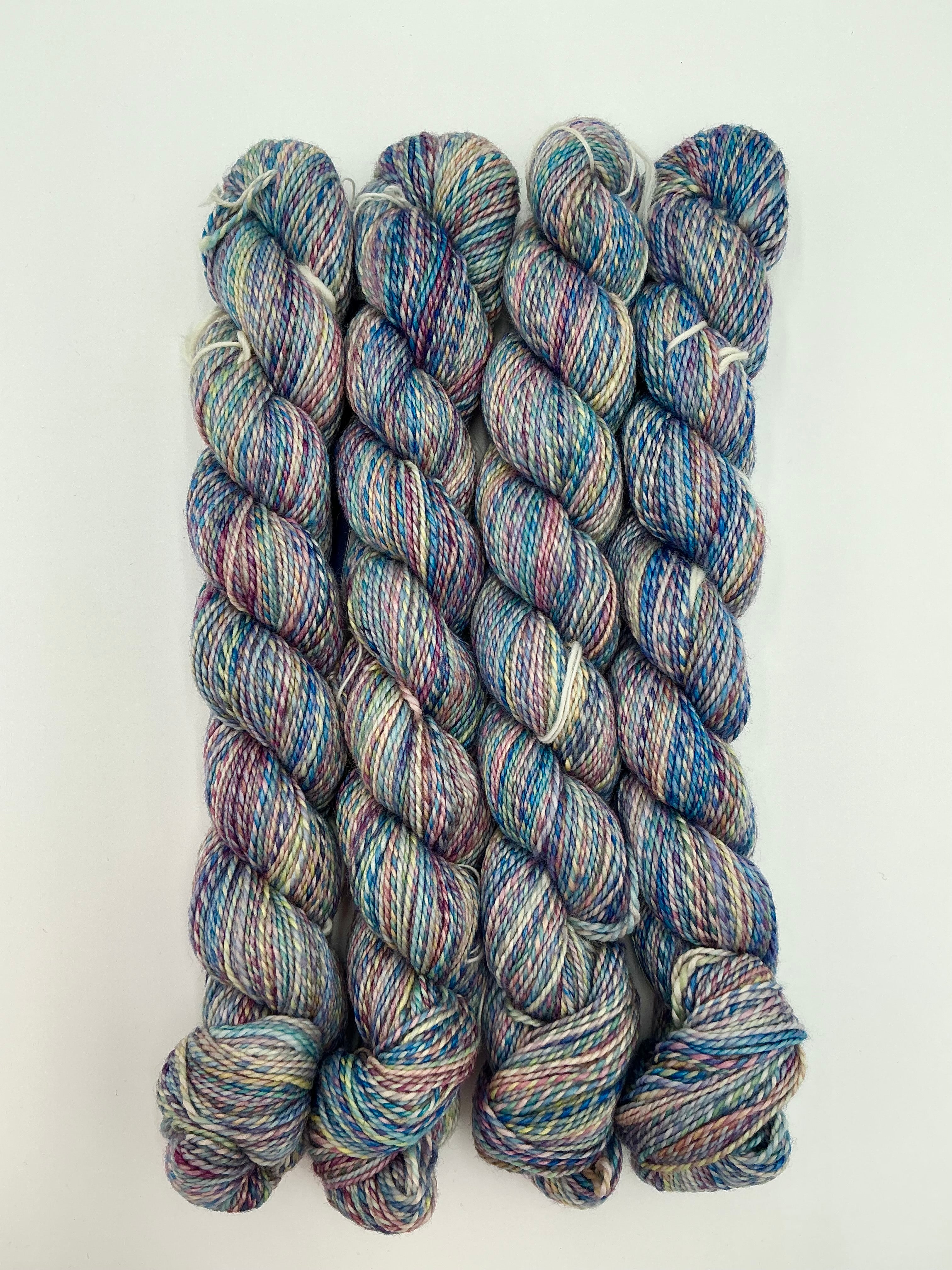 Four skeins of variegated yarn with a blend of blue, purple, pink, and green tones, arranged vertically on a plain white background.