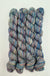 Four skeins of variegated yarn with a blend of blue, purple, pink, and green tones, arranged vertically on a plain white background.